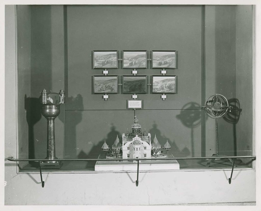 Close-up view of a display case of historic scientific instruments on the mid-level of the Adler Planetarium. Display case includes six landscape paintings painted by Charles Woodbury during an August 1932 eclipse. Courtesy: Adler Planetarium
